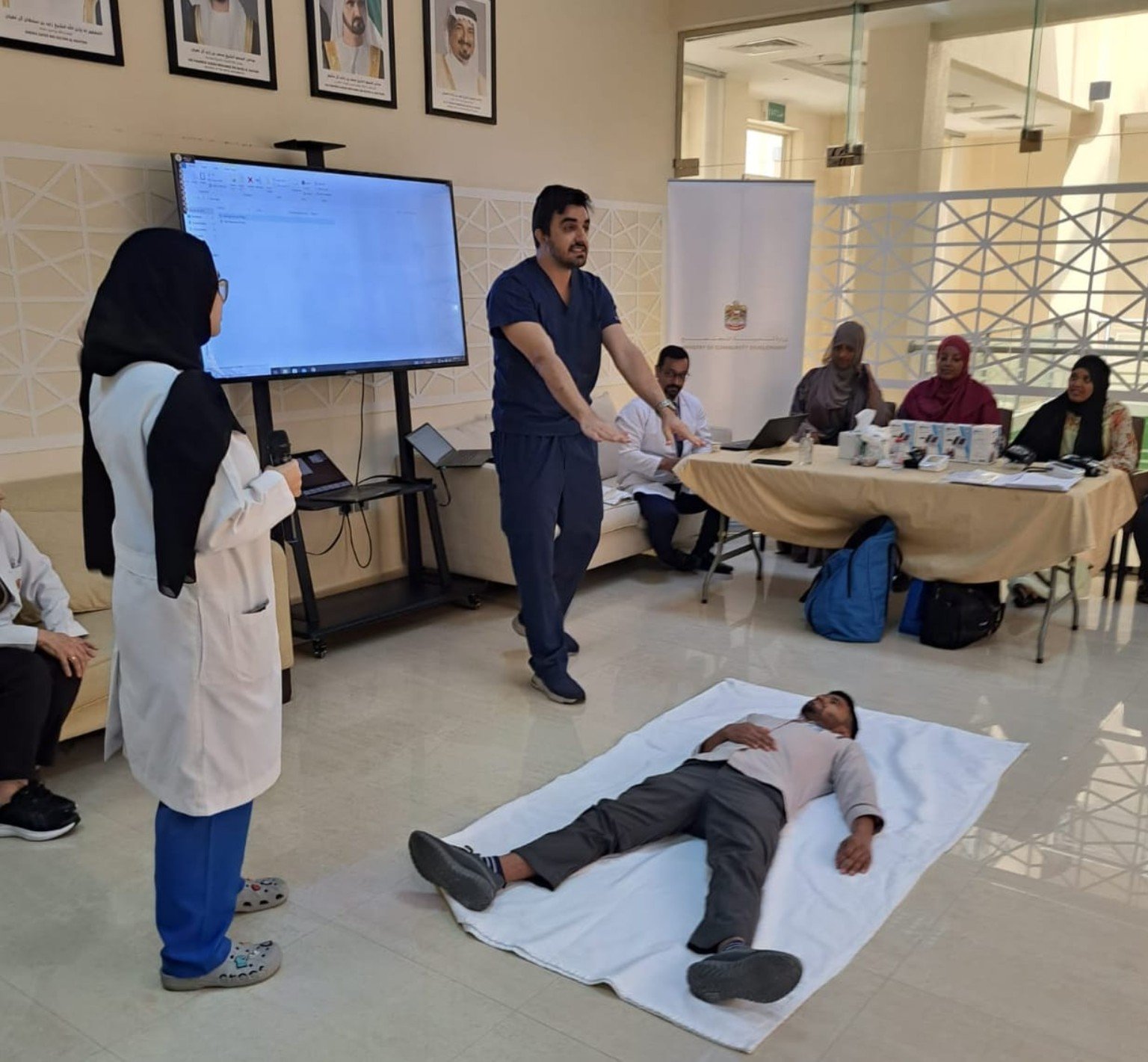 Dr. Alireza Amin explaining a first-aid exercise beside a participant lying on a training mat